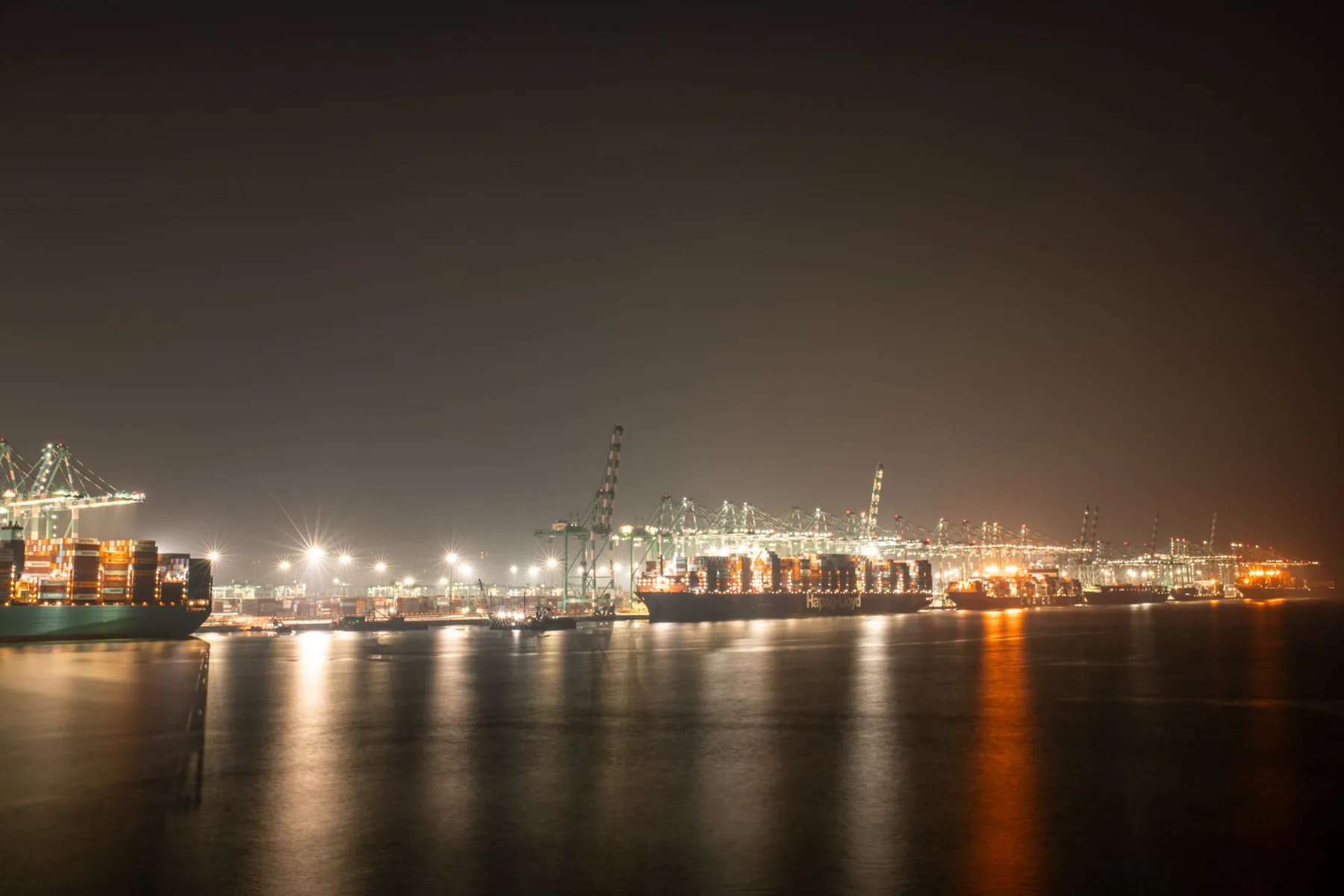 Port de commerce illuminé à la tombée de la nuit, grues et navires